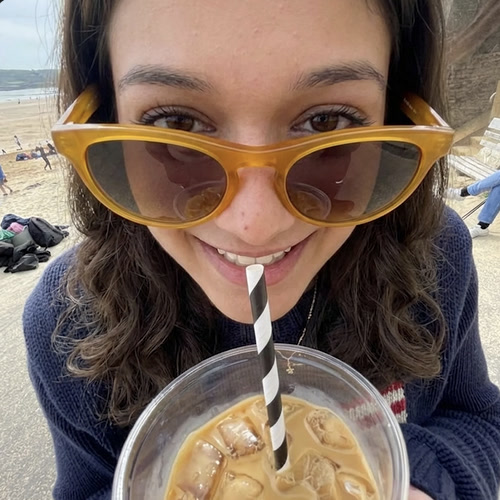 Maahira at the beach with sunglasses and an iced coffee